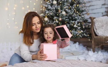 37 Best Christmas Gifts for Mom She’ll Actually Use Mother and daughter opening a Christmas gift by the tree