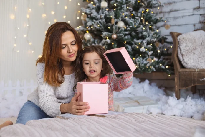 Mother and daughter opening a Christmas gift by the tree