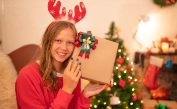 35 Best Gifts for Teenage Girls She’ll Actually Love Teenage girl holding a Christmas gift by the tree